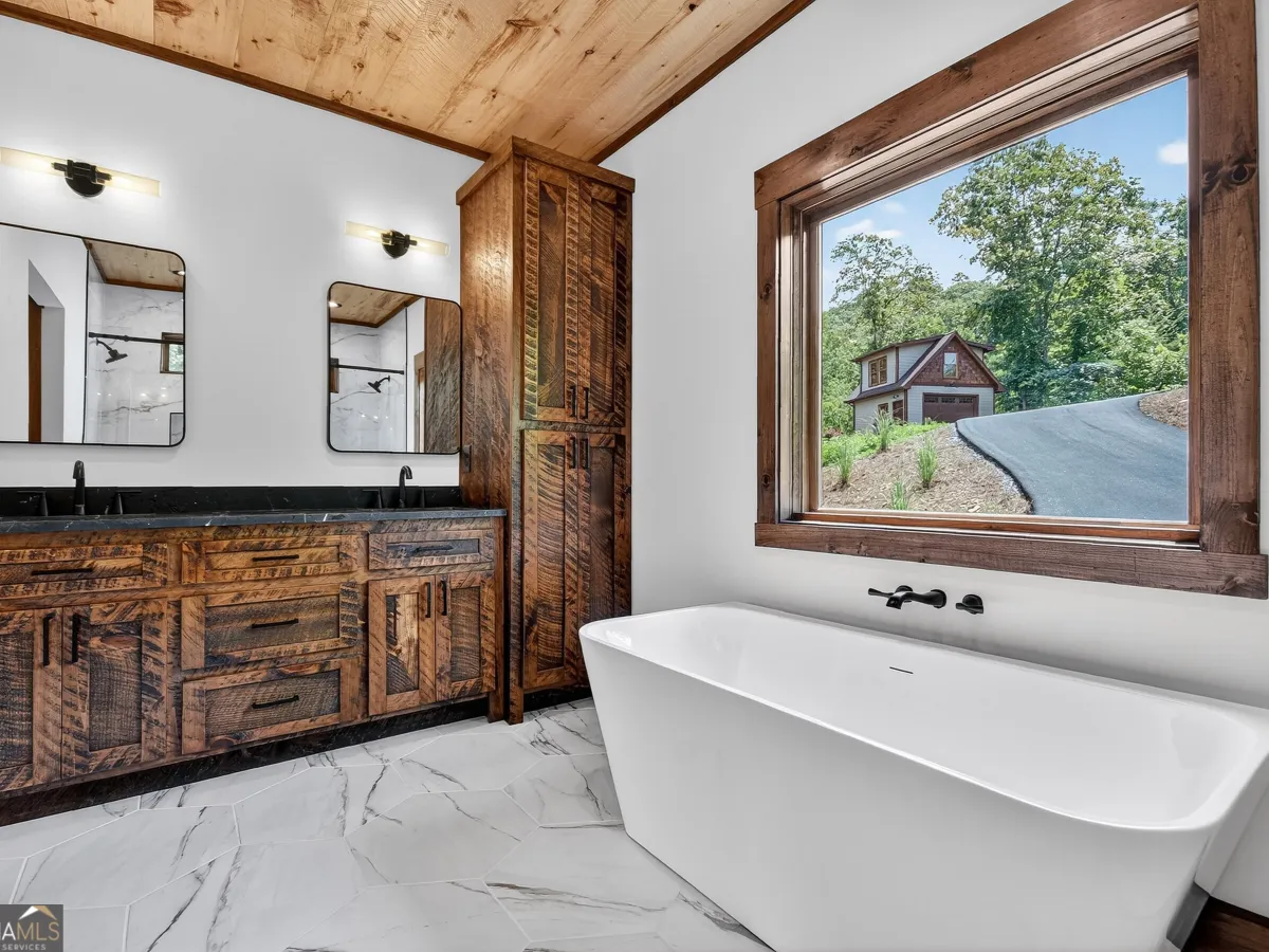Modern bathroom with marble floors, a double wooden vanity, a freestanding tub, and a window with a mountain view.