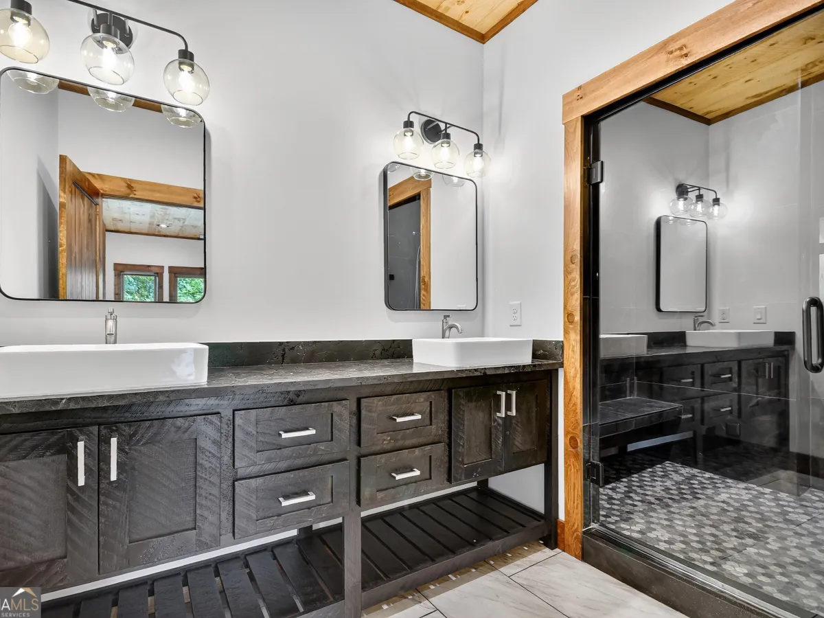 A dual-sink bathroom vanity with dark wood cabinets, white basins, modern mirrors, and a glass-enclosed shower.