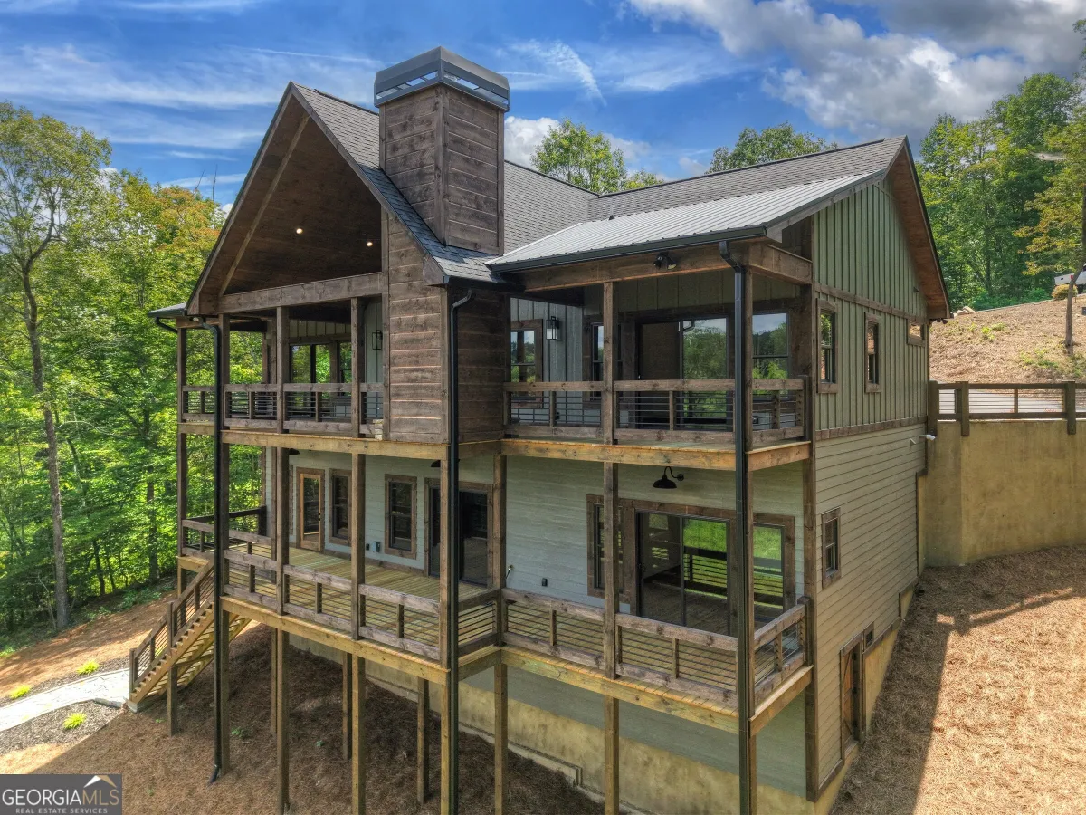 A multi-story cabin with a large stone chimney, wrap-around wooden decks, and light green siding in a wooded setting.