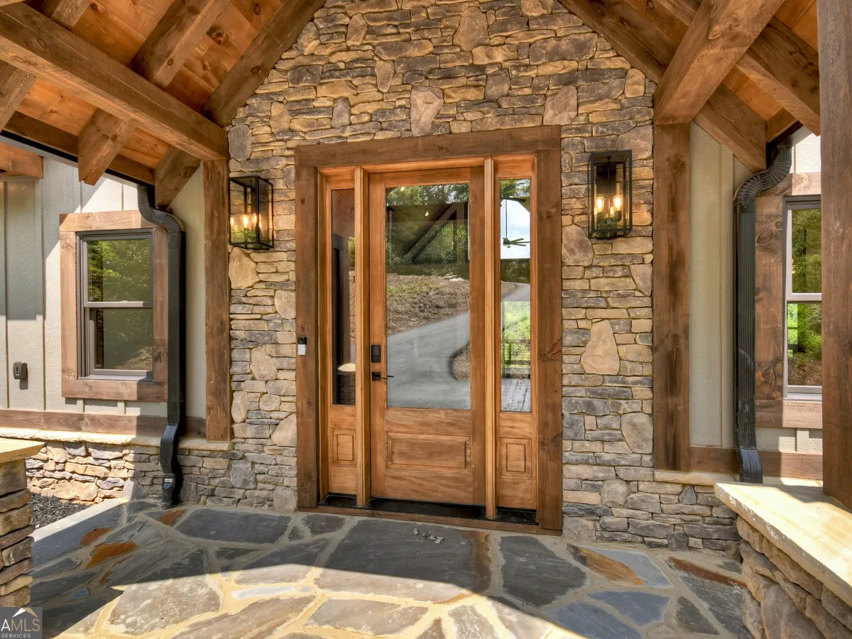 Rustic wooden front door with glass panels, framed by stone walls and timber beams on a slate-tiled entryway porch.