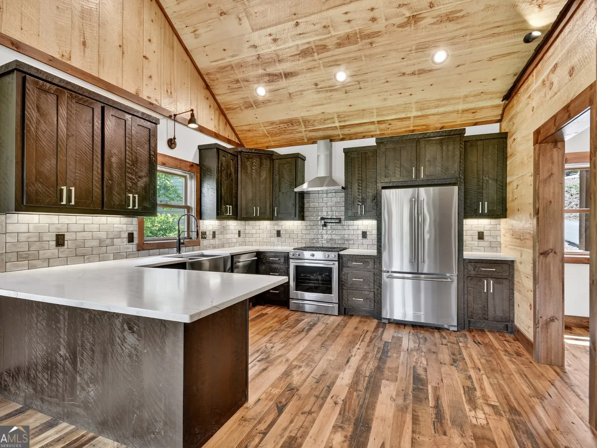 A rustic-style kitchen featuring dark wood cabinetry, stainless steel appliances, a white island, and wood-paneled ceiling.