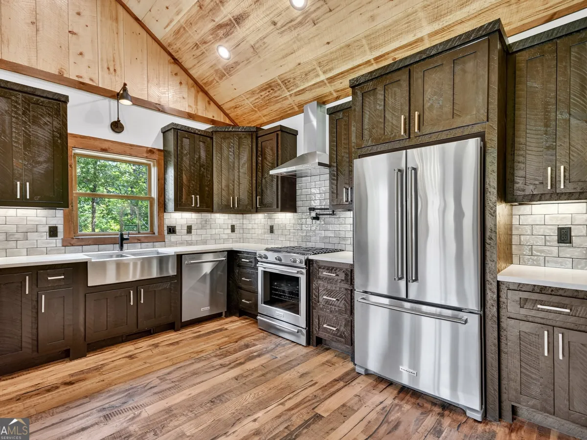 A modern rustic kitchen with dark wood cabinets, stainless steel appliances, a farmhouse sink, and a wood-paneled ceiling.