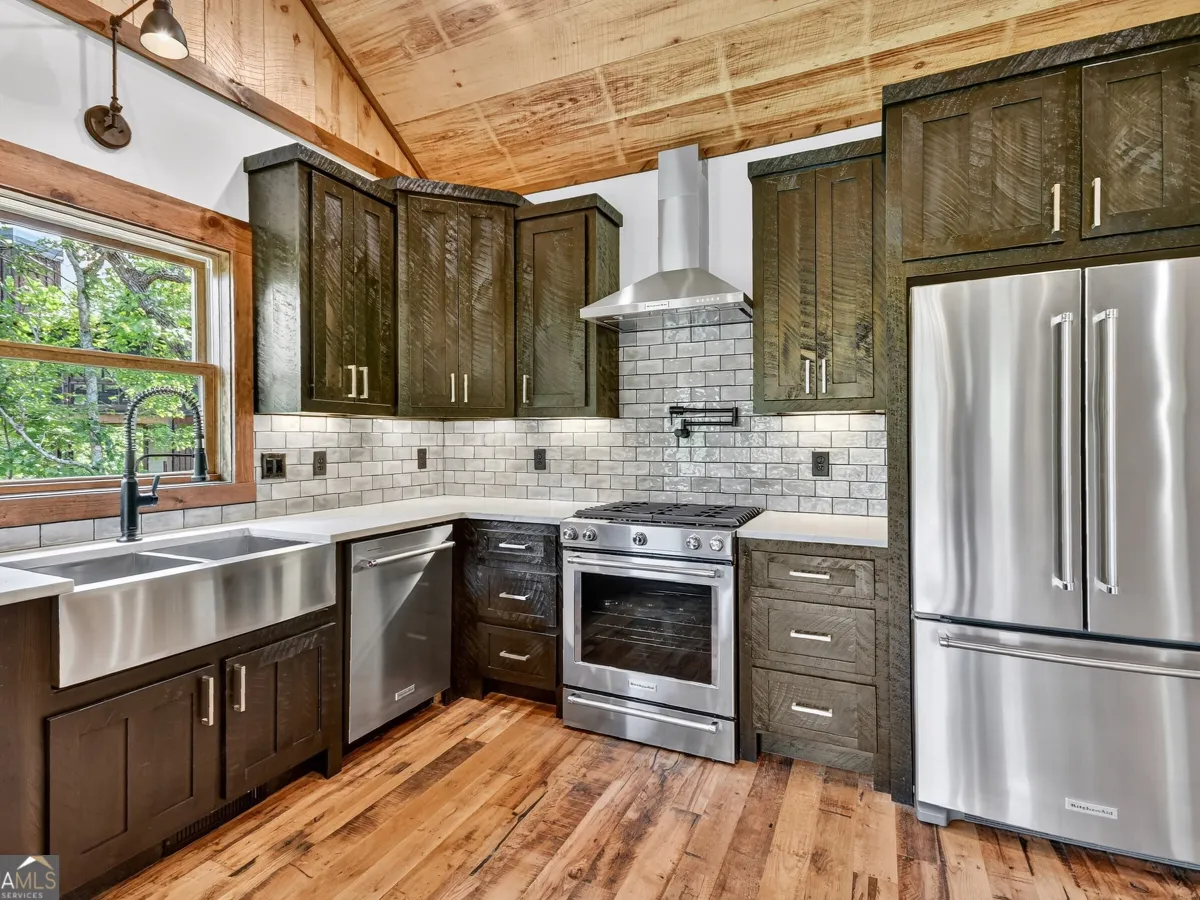 A rustic kitchen featuring dark wood cabinets, stainless steel appliances, a farmhouse sink, and a light-brick backsplash.