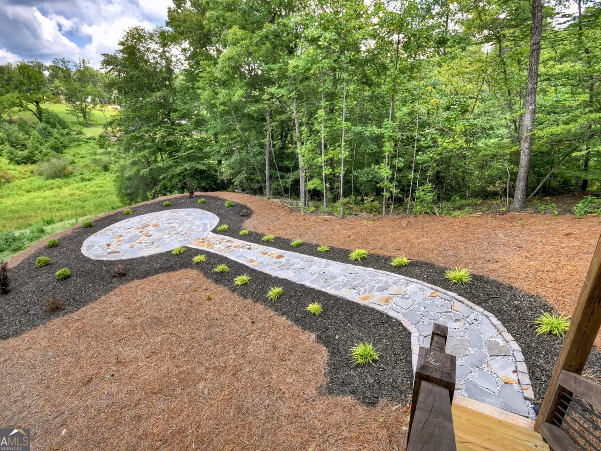 A stone patio and path surrounded by dark mulch and small green plants, set against a background of lush trees.