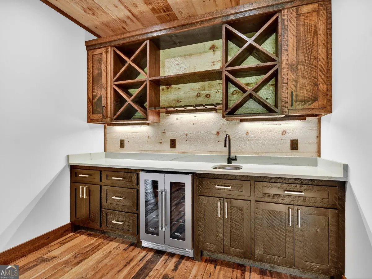 A rustic wet bar with wooden cabinets, X-frame wine storage, a built-in wine cooler, and a white countertop.