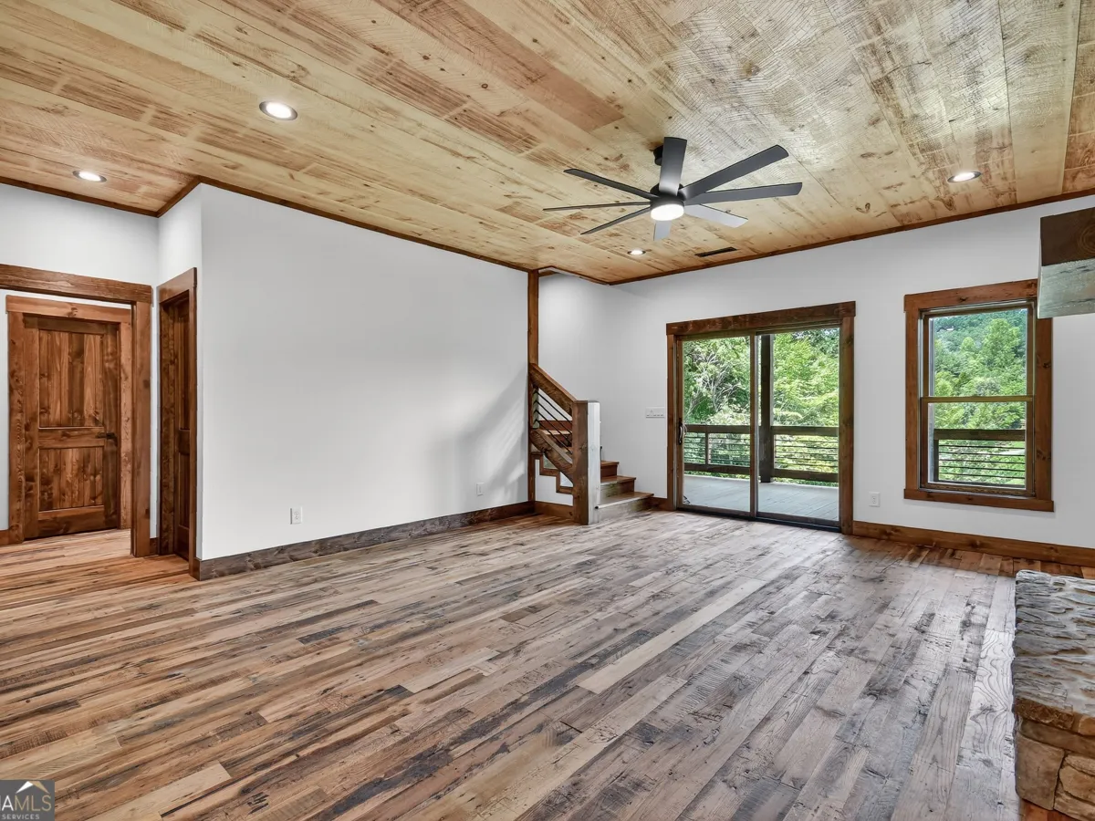 A spacious, rustic-style room with wood-plank ceilings and flooring, a wooden staircase, sliding glass doors, and a window.