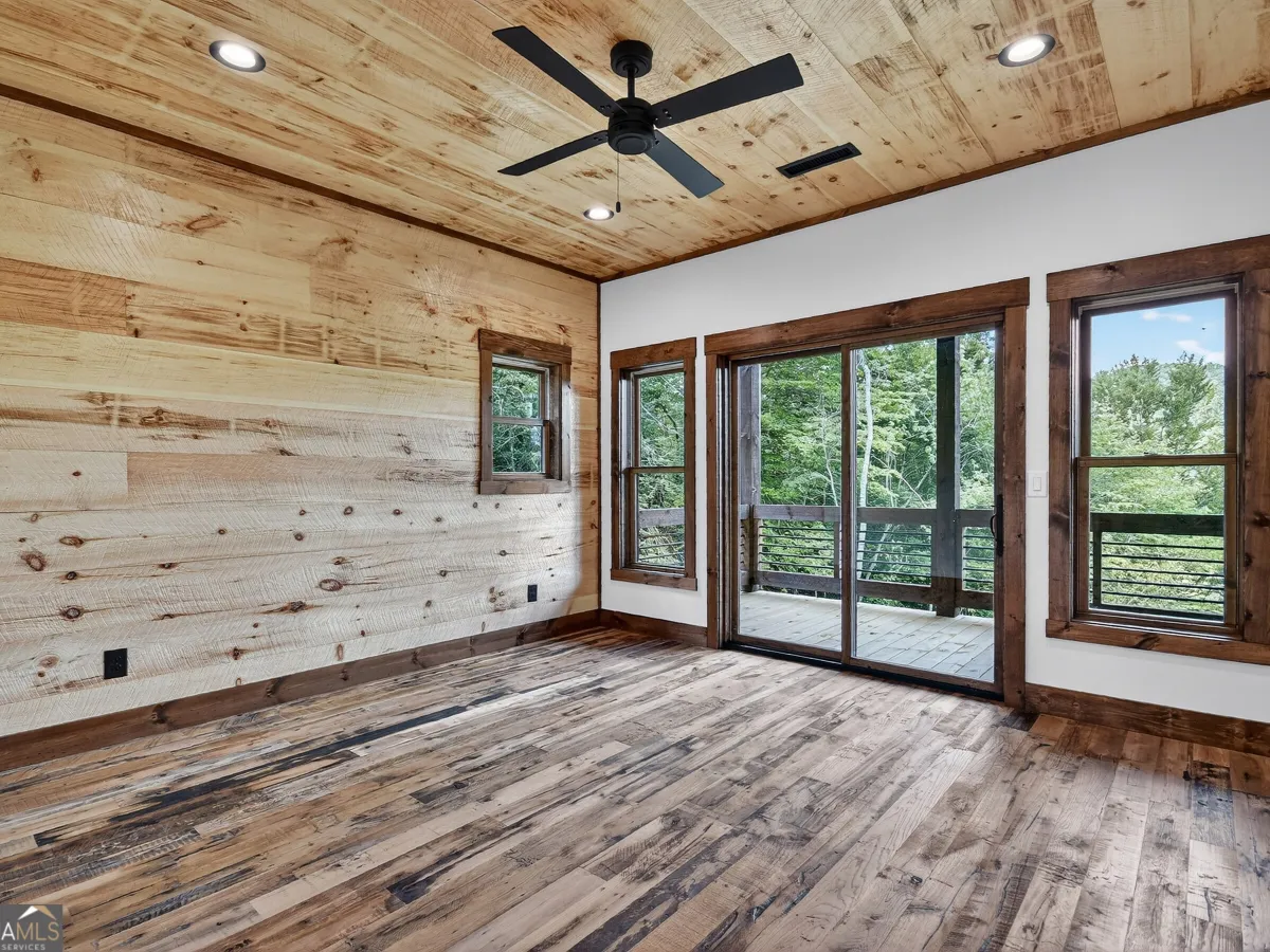 An empty room with rustic wood paneling on the walls and ceiling, dark hardwood floors, a ceiling fan, and sliding doors.