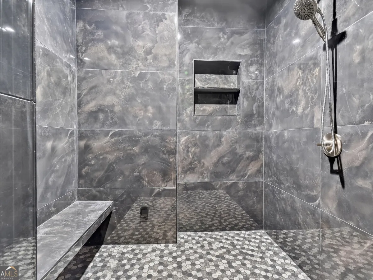 A modern shower with large, grey, marble-patterned wall tiles, a pebble floor, a built-in bench, and a wall niche.