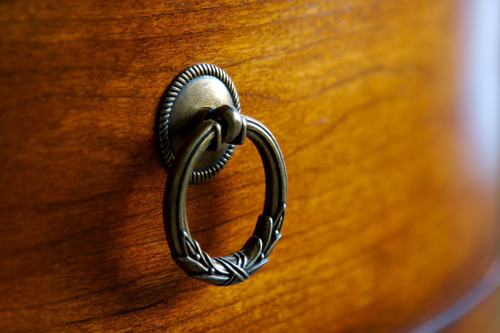 A close up of a brass handle on a wooden cabinet.
