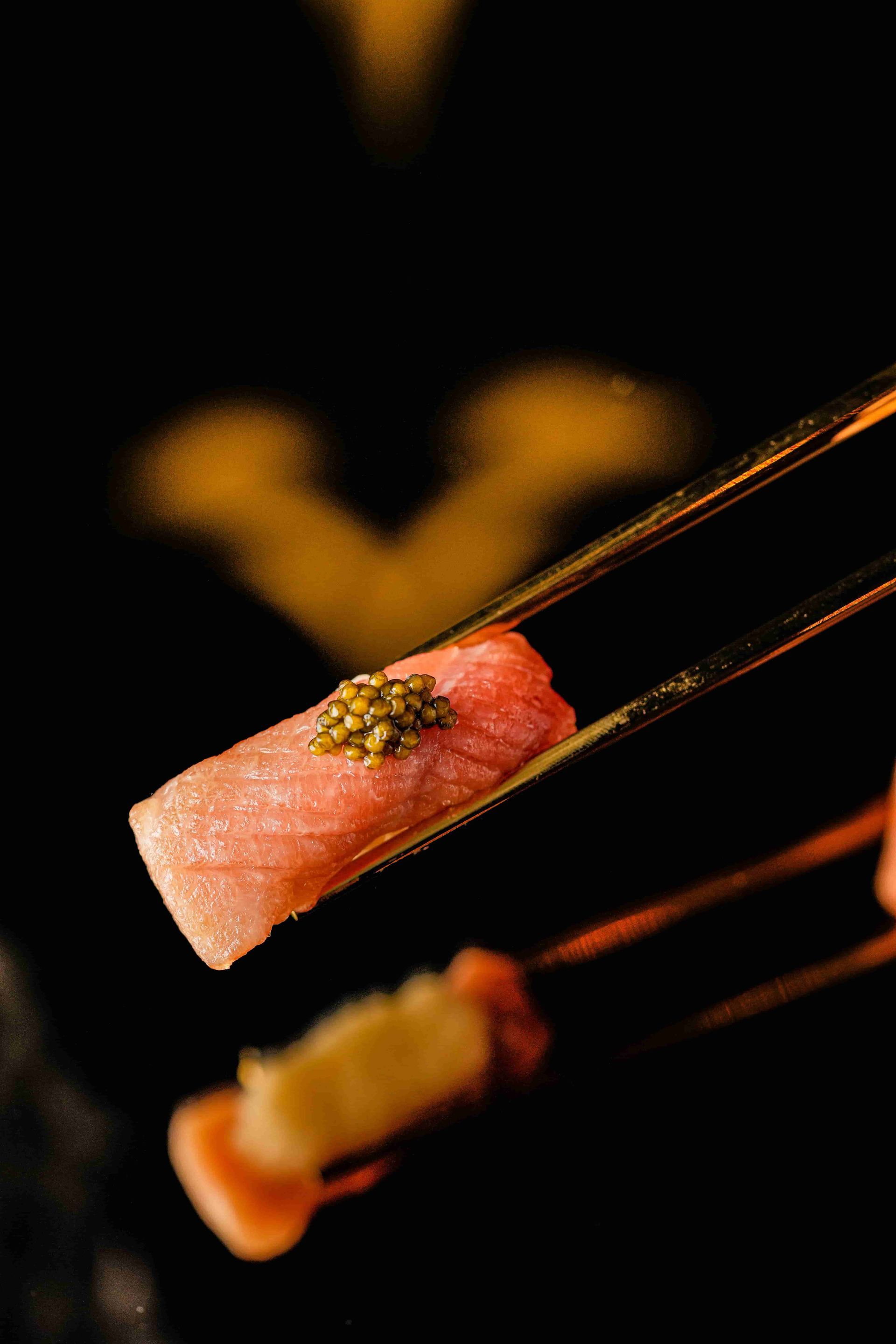 Piece of salmon and fish eggs held by chop sticks