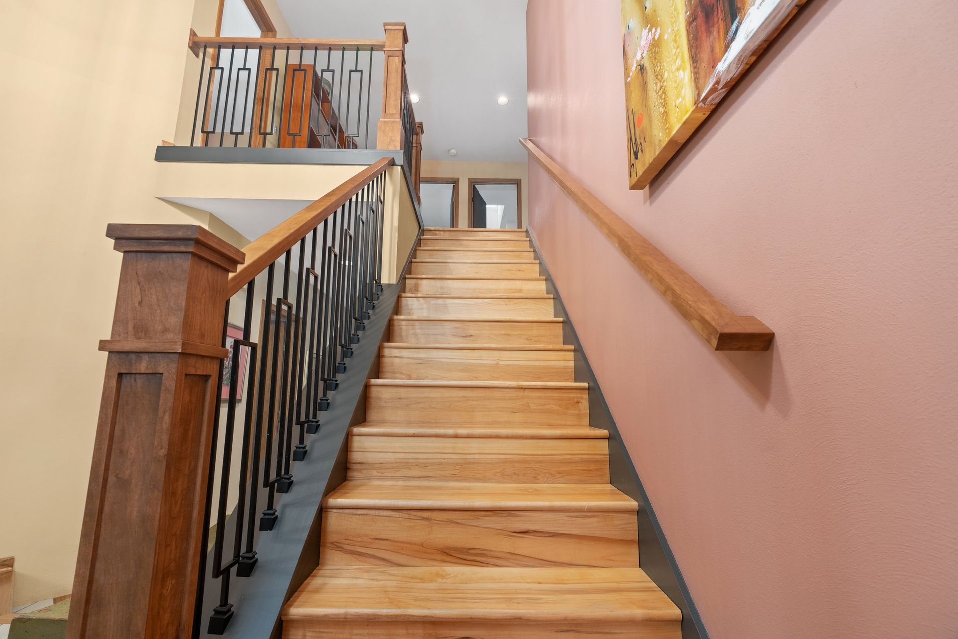 A wooden staircase with a metal railing and a painting on the wall.