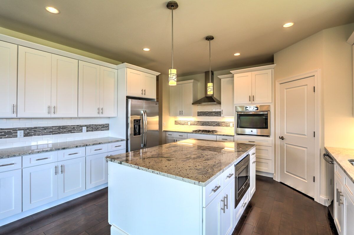 A kitchen with white cabinets , granite counter tops , stainless steel appliances and a large island.