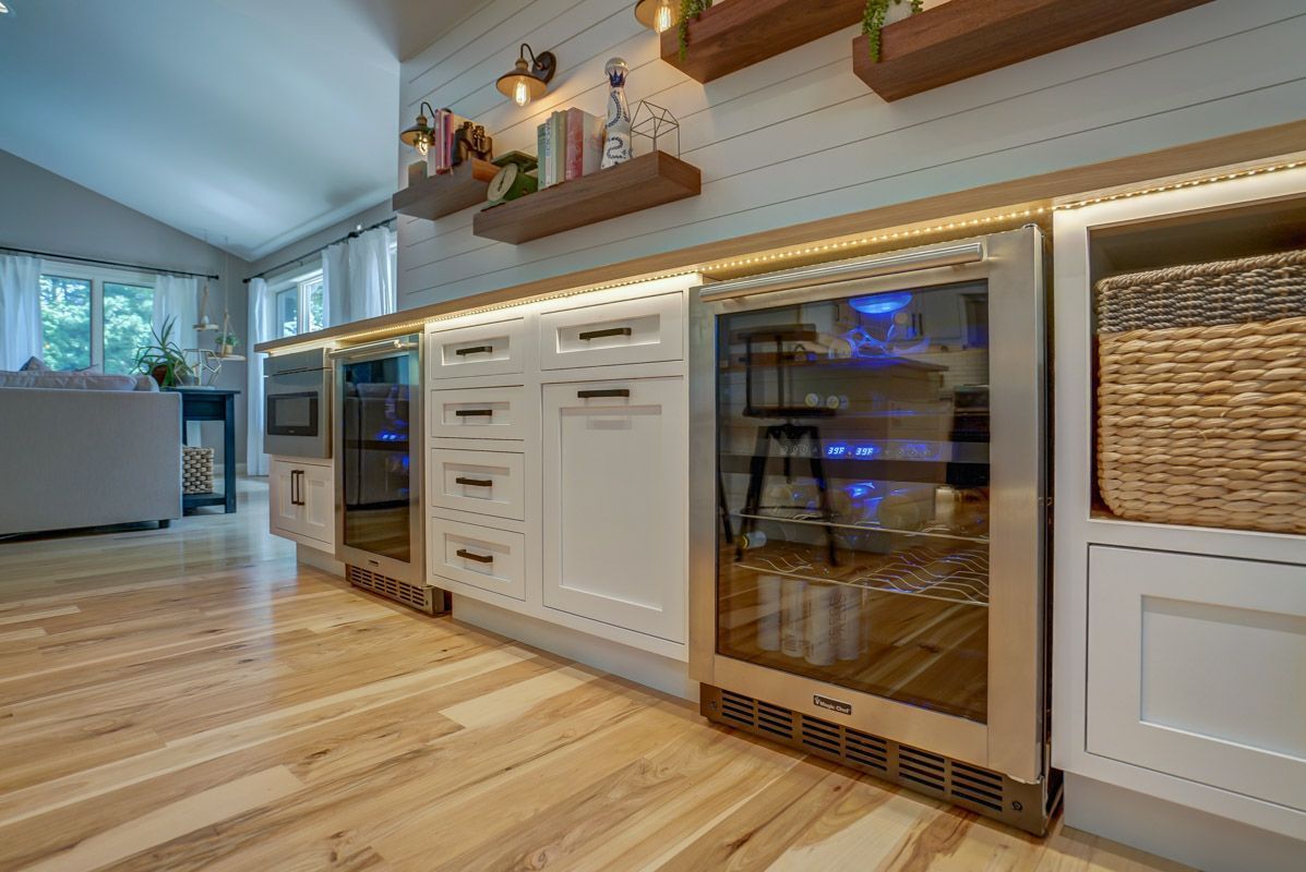A kitchen with hardwood floors , white cabinets , stainless steel appliances and a wine cooler.