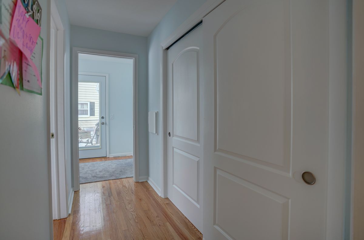A hallway with hardwood floors and white doors leading to a bedroom