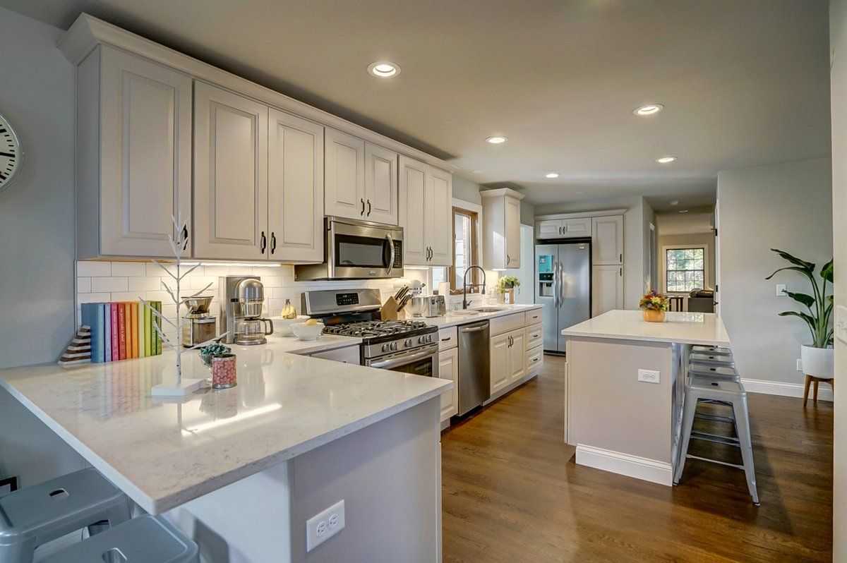 A kitchen with white cabinets , stainless steel appliances , a large island and a clock on the wall.