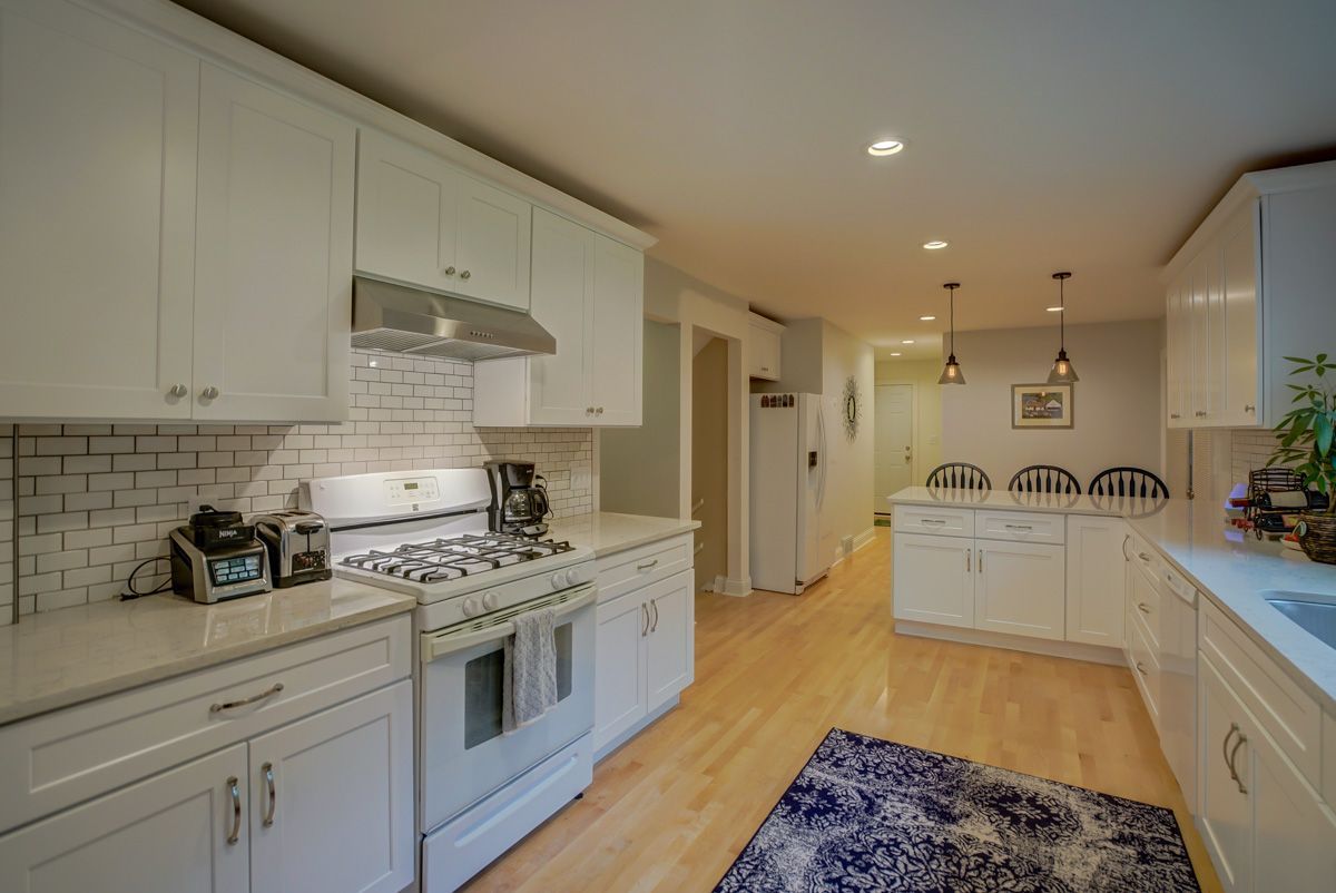A kitchen with white cabinets , a stove , a refrigerator , and a rug.