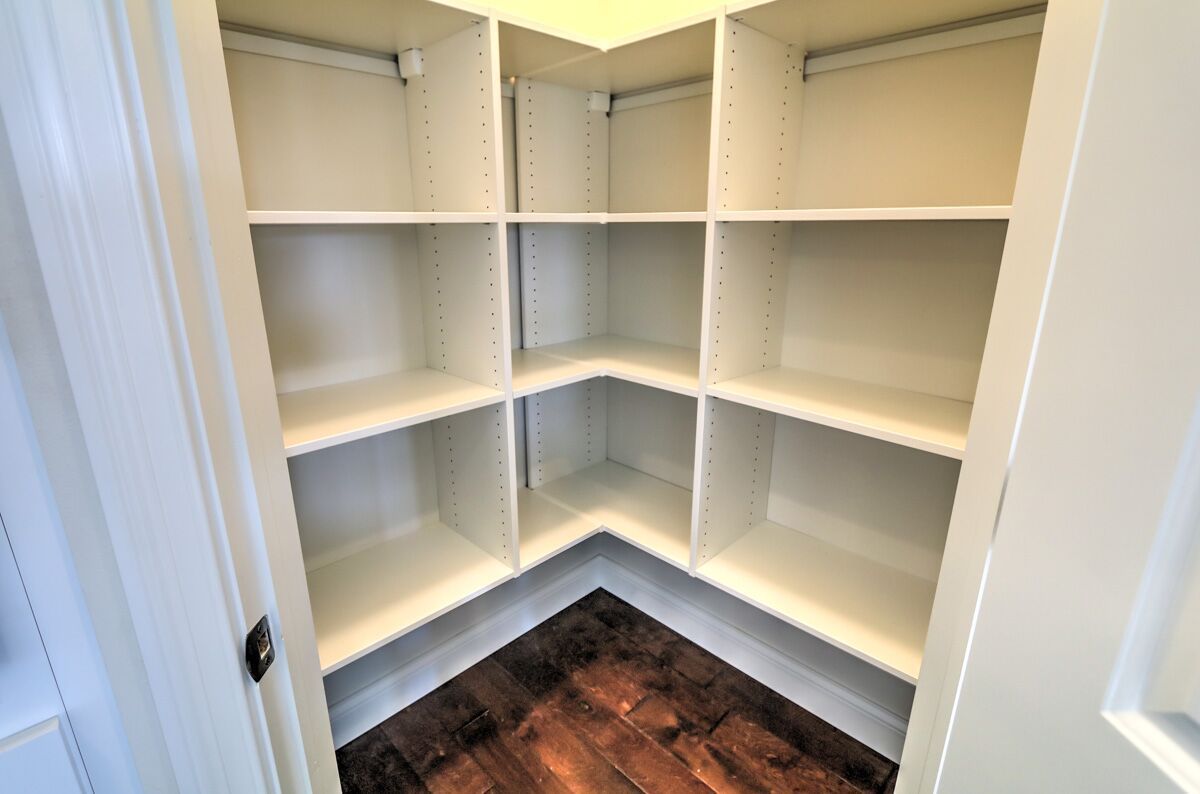 An empty pantry with white shelves and wooden floors.