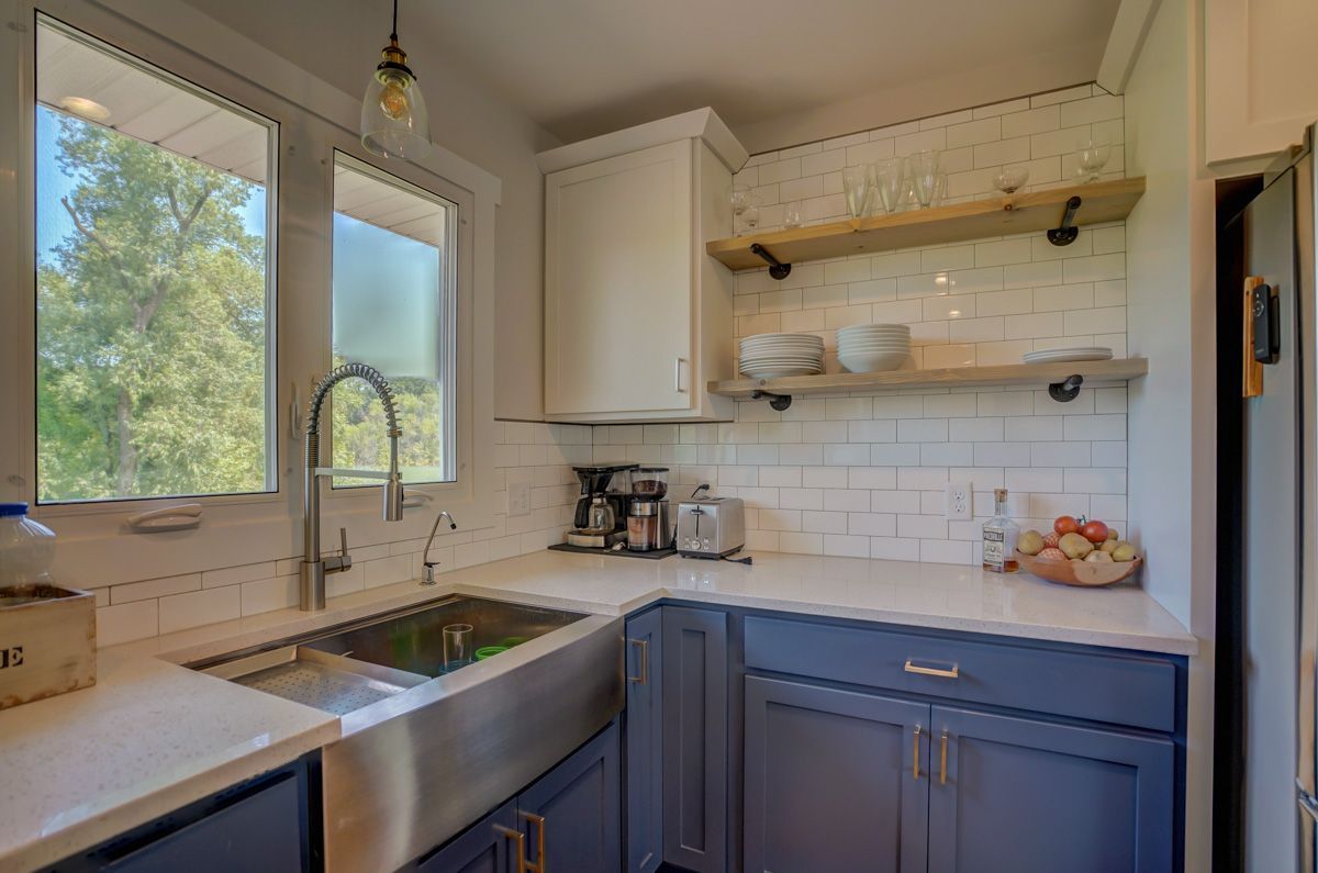 A kitchen with a sink , cabinets , shelves and a window.