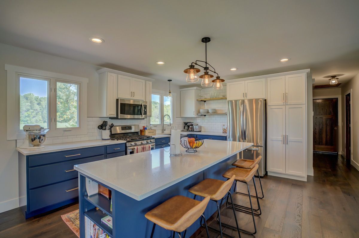 A kitchen with blue cabinets , white counter tops , stainless steel appliances and a large island.