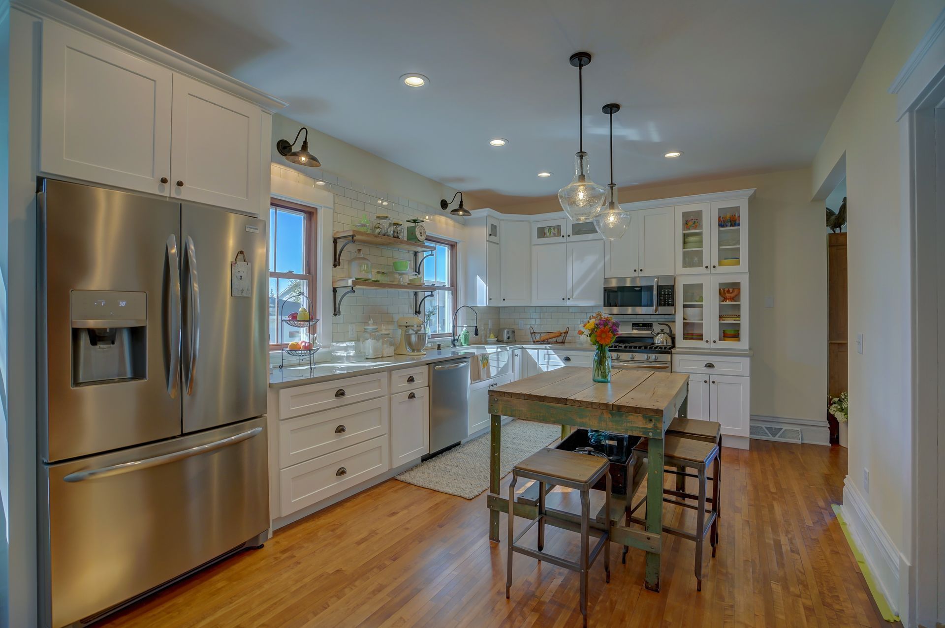 A kitchen with stainless steel appliances , white cabinets , hardwood floors and a table.