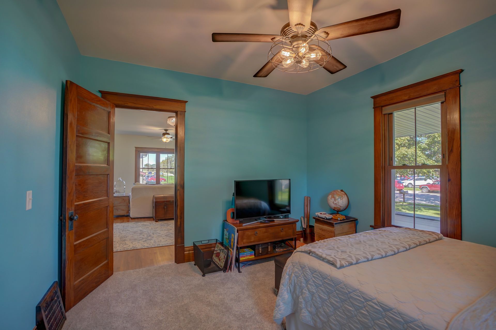 A bedroom with blue walls , a bed , a television and a ceiling fan.