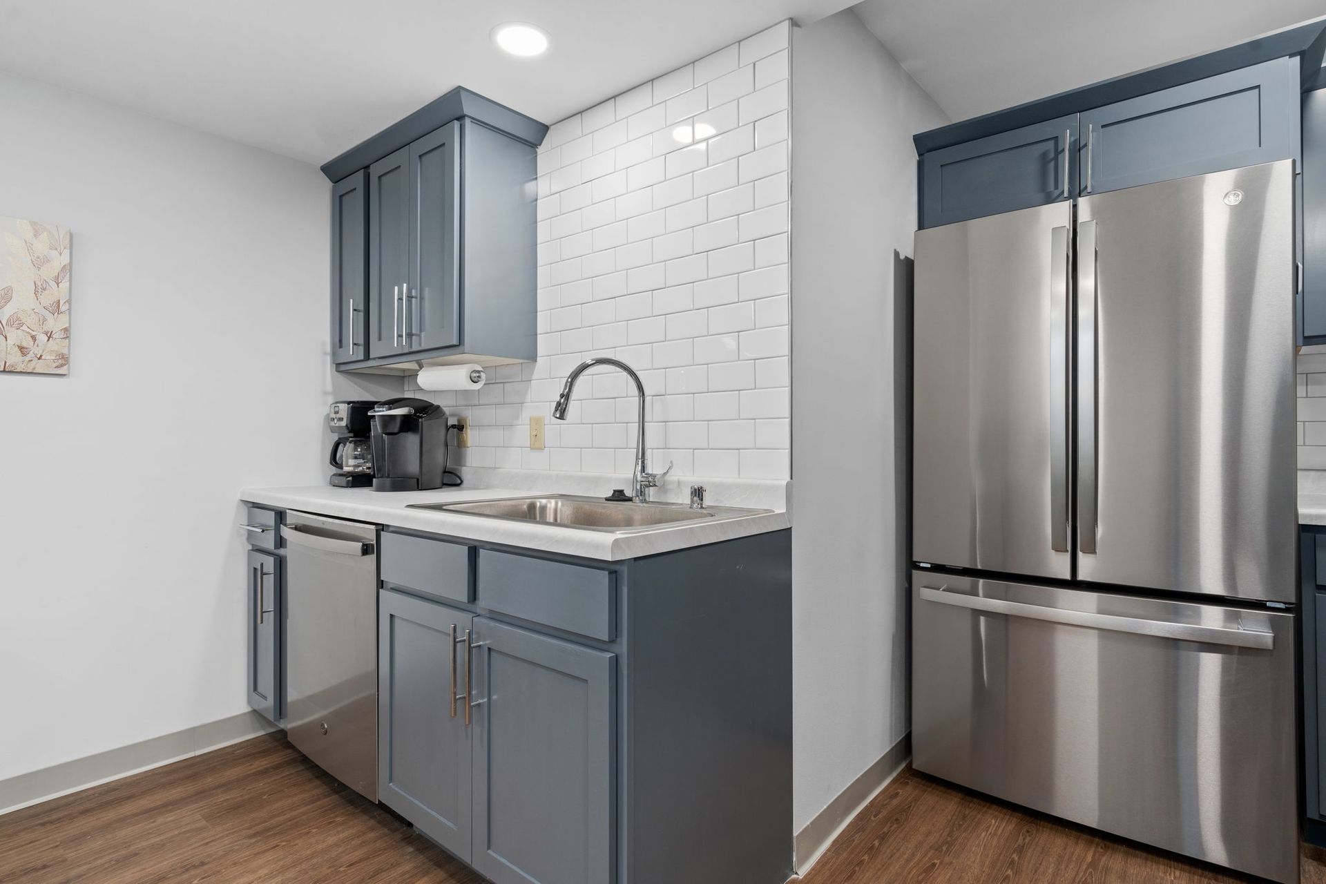 A kitchen with stainless steel appliances , blue cabinets , a sink , and a refrigerator.