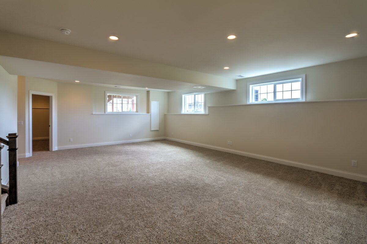An empty basement with a carpeted floor and two windows.