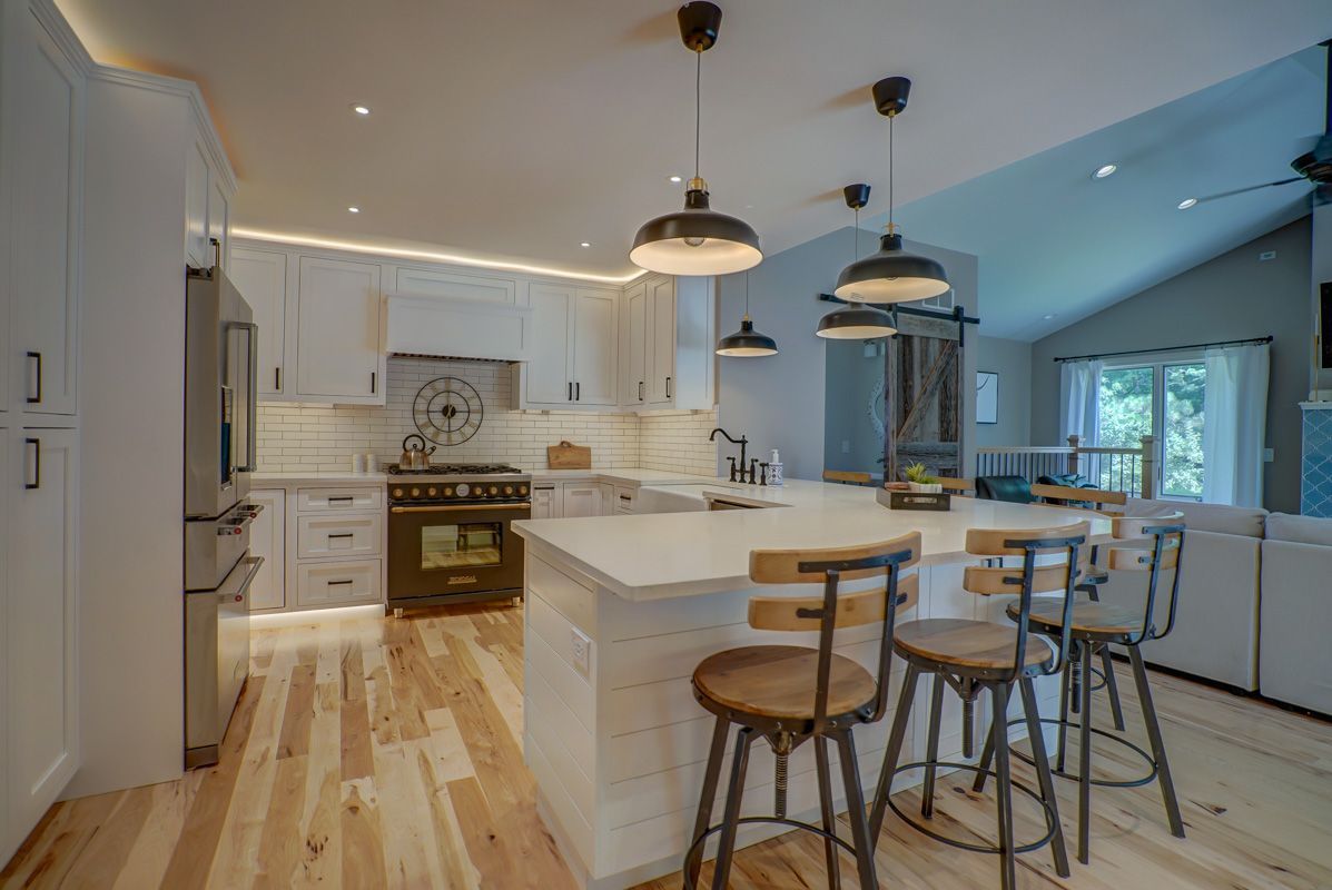 A kitchen with white cabinets , wooden floors , stools and a large island.