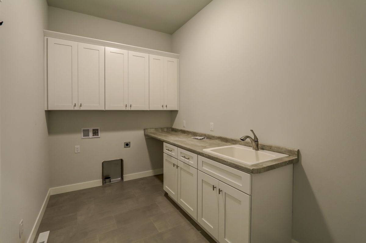 A laundry room with white cabinets and a sink.