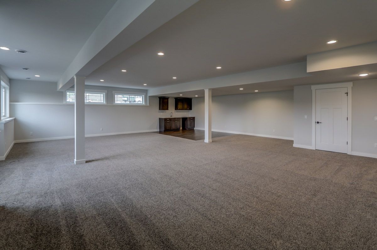 An empty basement with a carpeted floor and a fireplace.