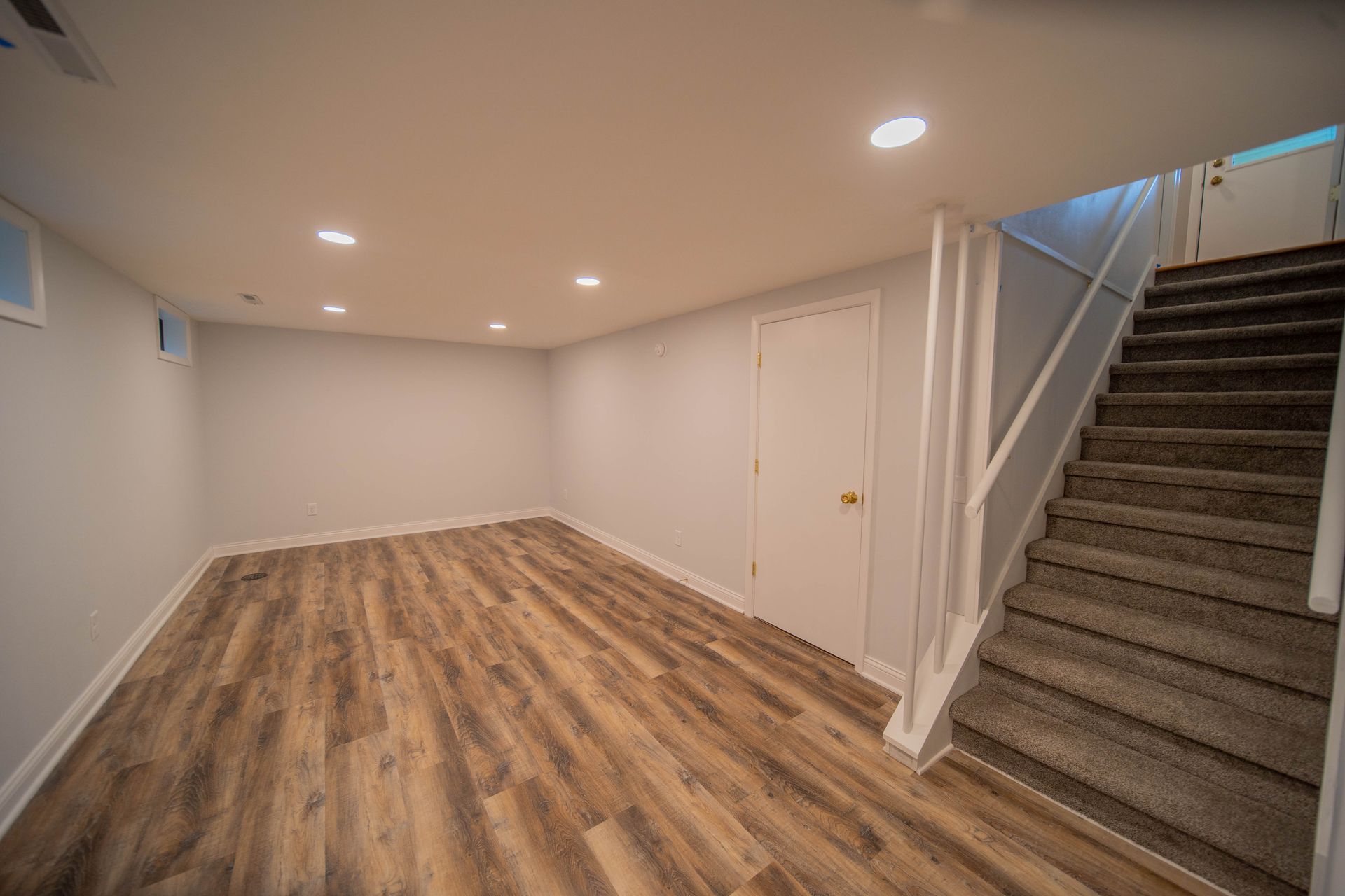An empty basement with hardwood floors and stairs leading up to the second floor.