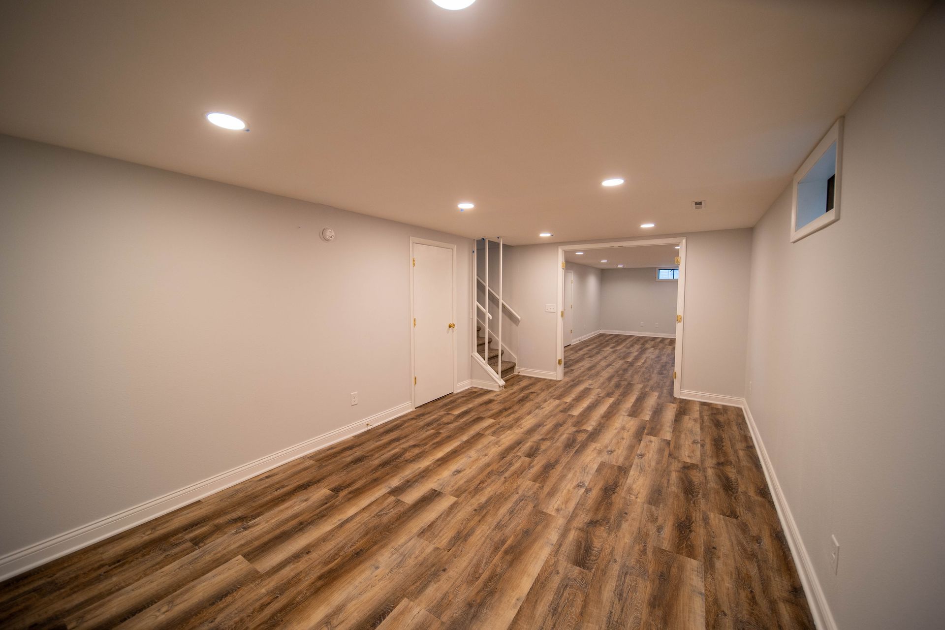 An empty basement with hardwood floors and white walls.