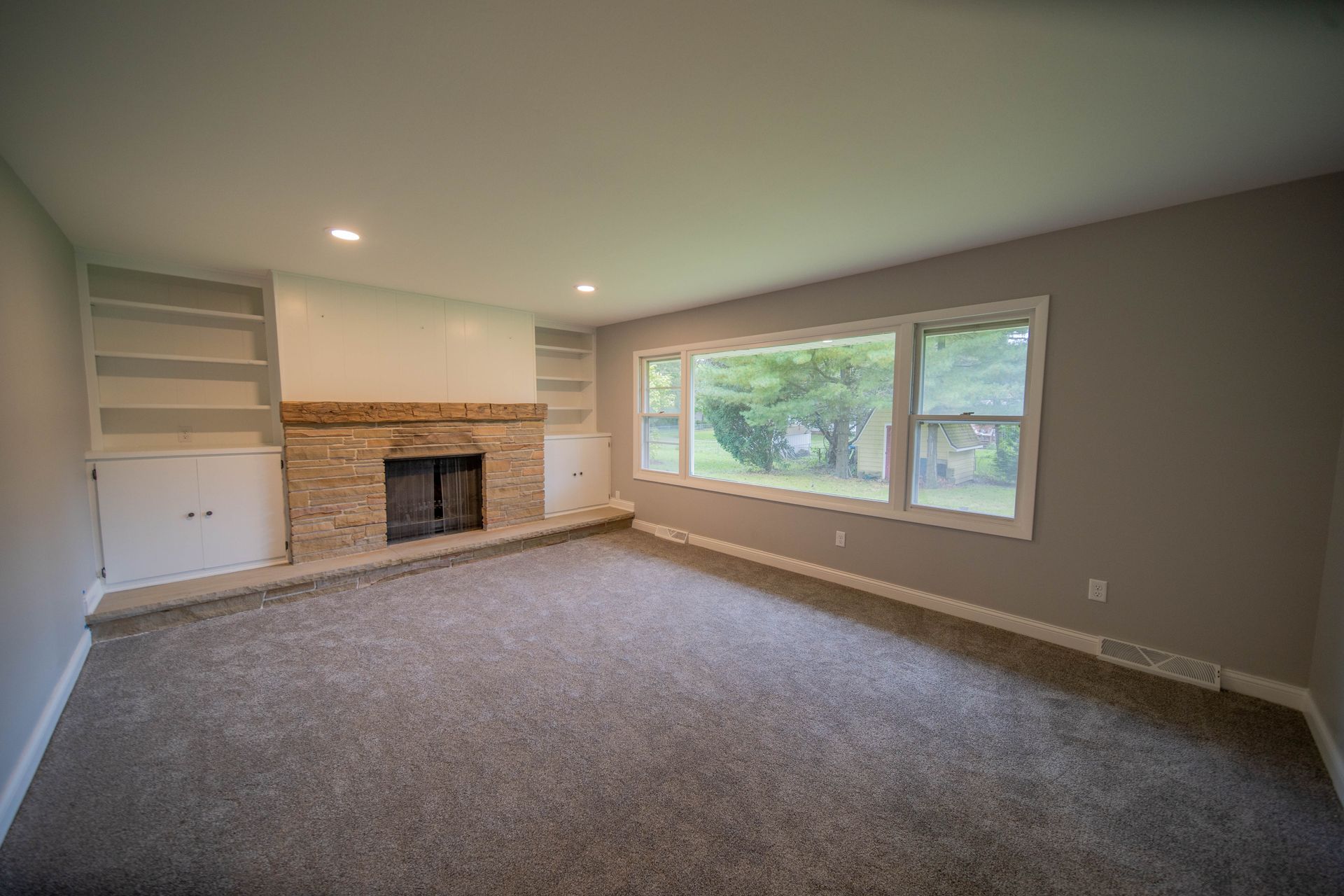 An empty living room with a fireplace and large windows.