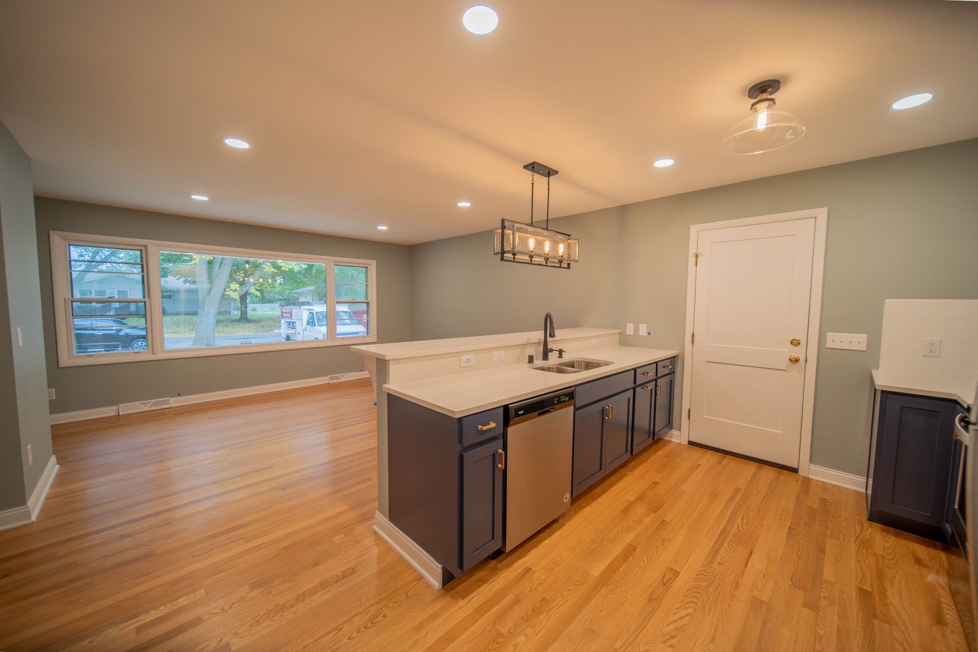 An empty kitchen with hardwood floors , stainless steel appliances , and a large island.
