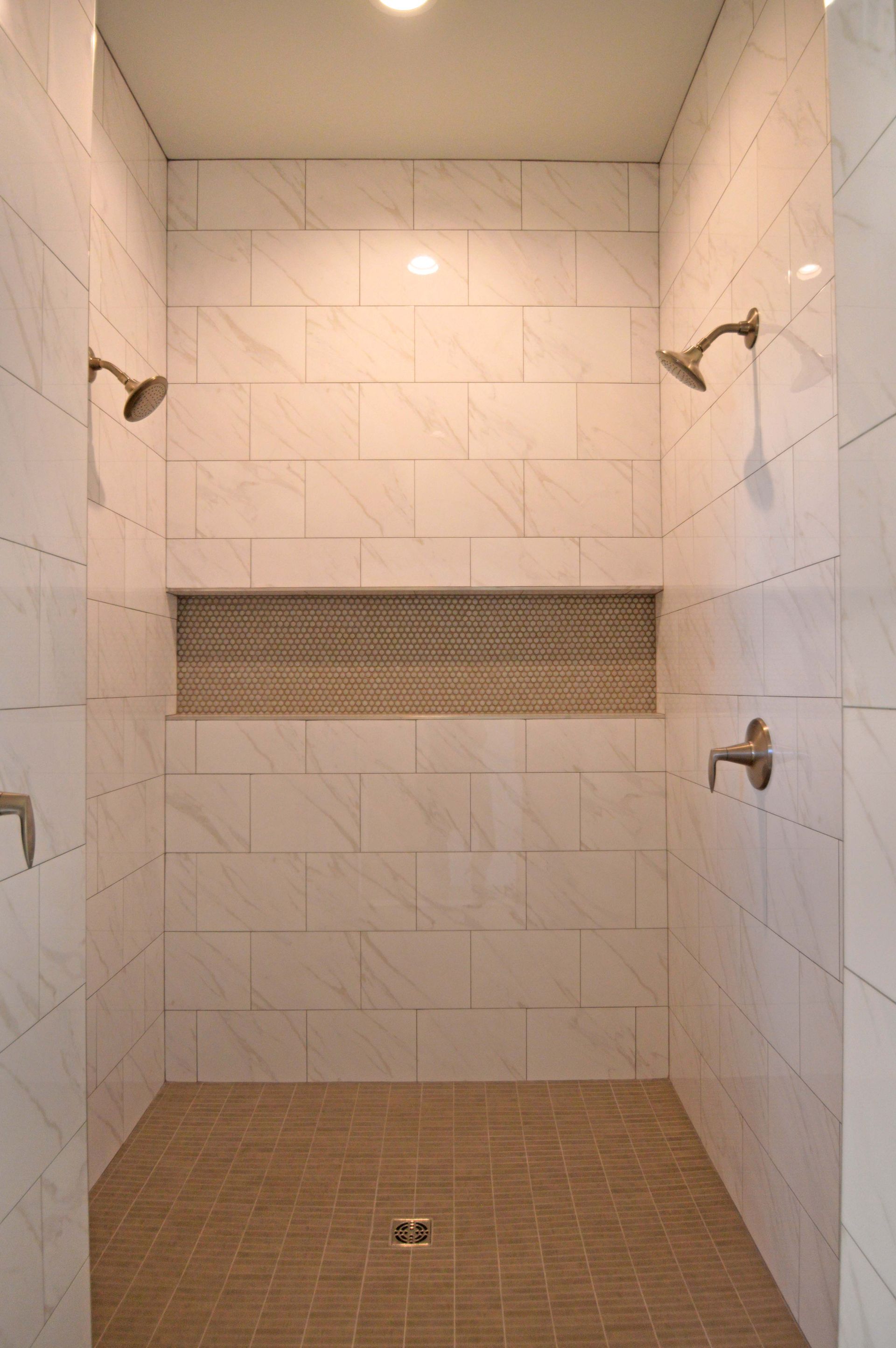 A walk in shower with two shower heads and a shelf.