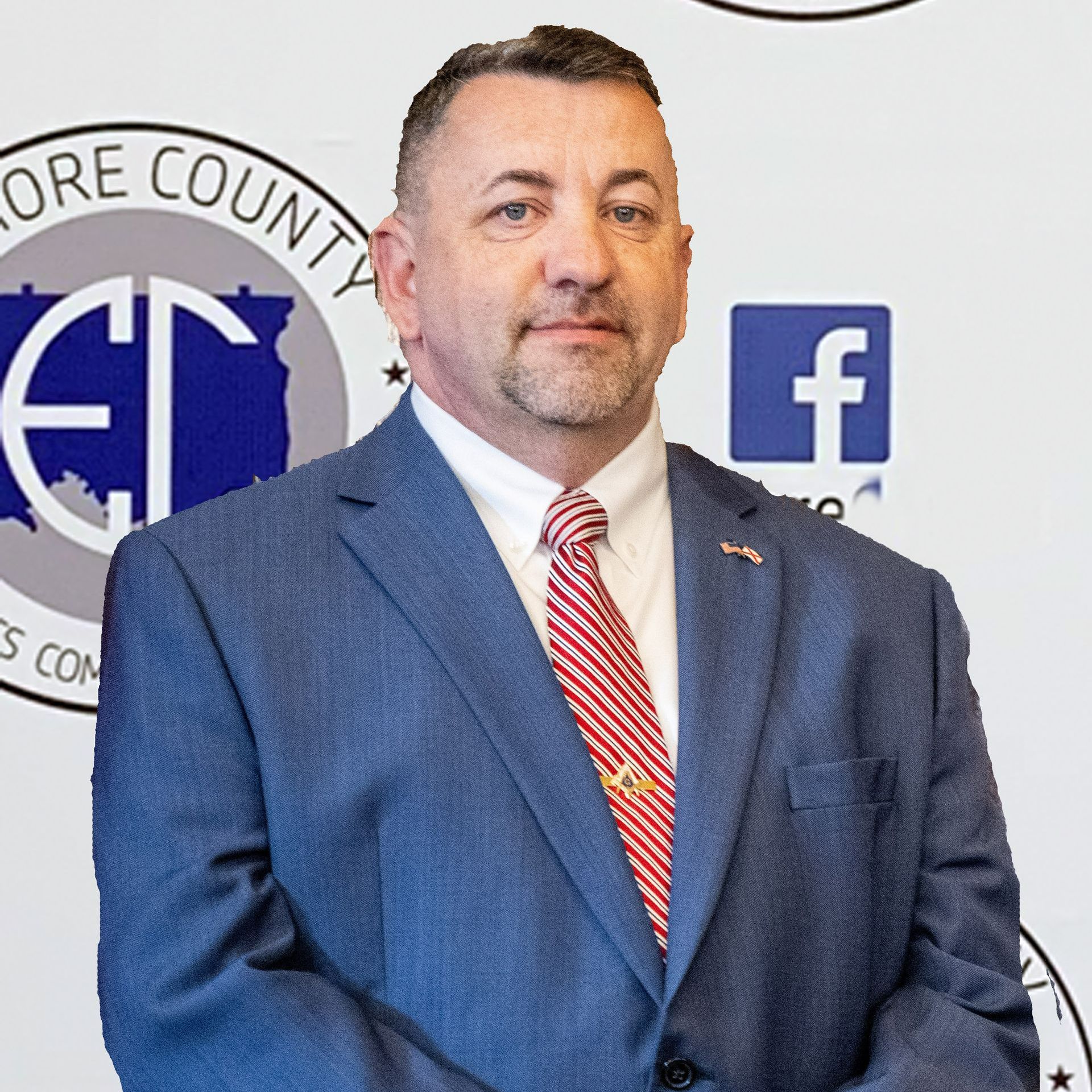 Man in a blue suit and red striped tie, standing in front of a backdrop with logos. He is looking at the camera.