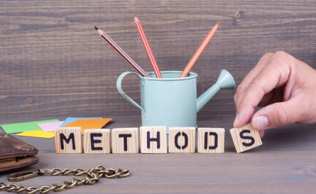 A person is holding wooden blocks that spell out the word methods