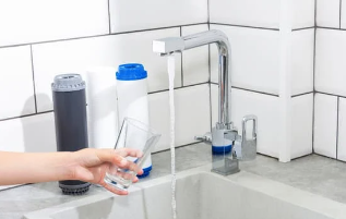 A person is pouring water from a faucet into a sink.