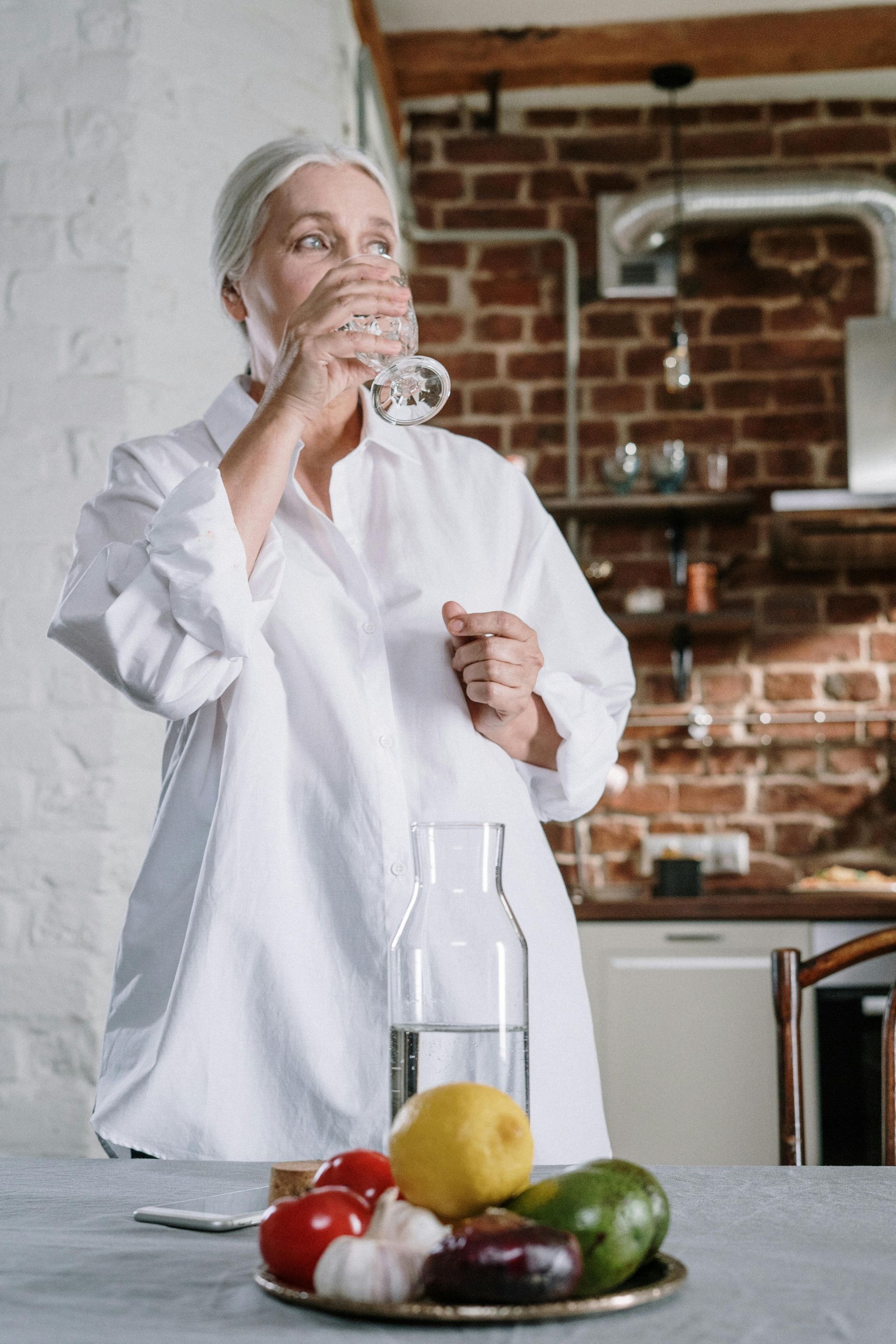 A woman is drinking a glass of water in a kitchen.