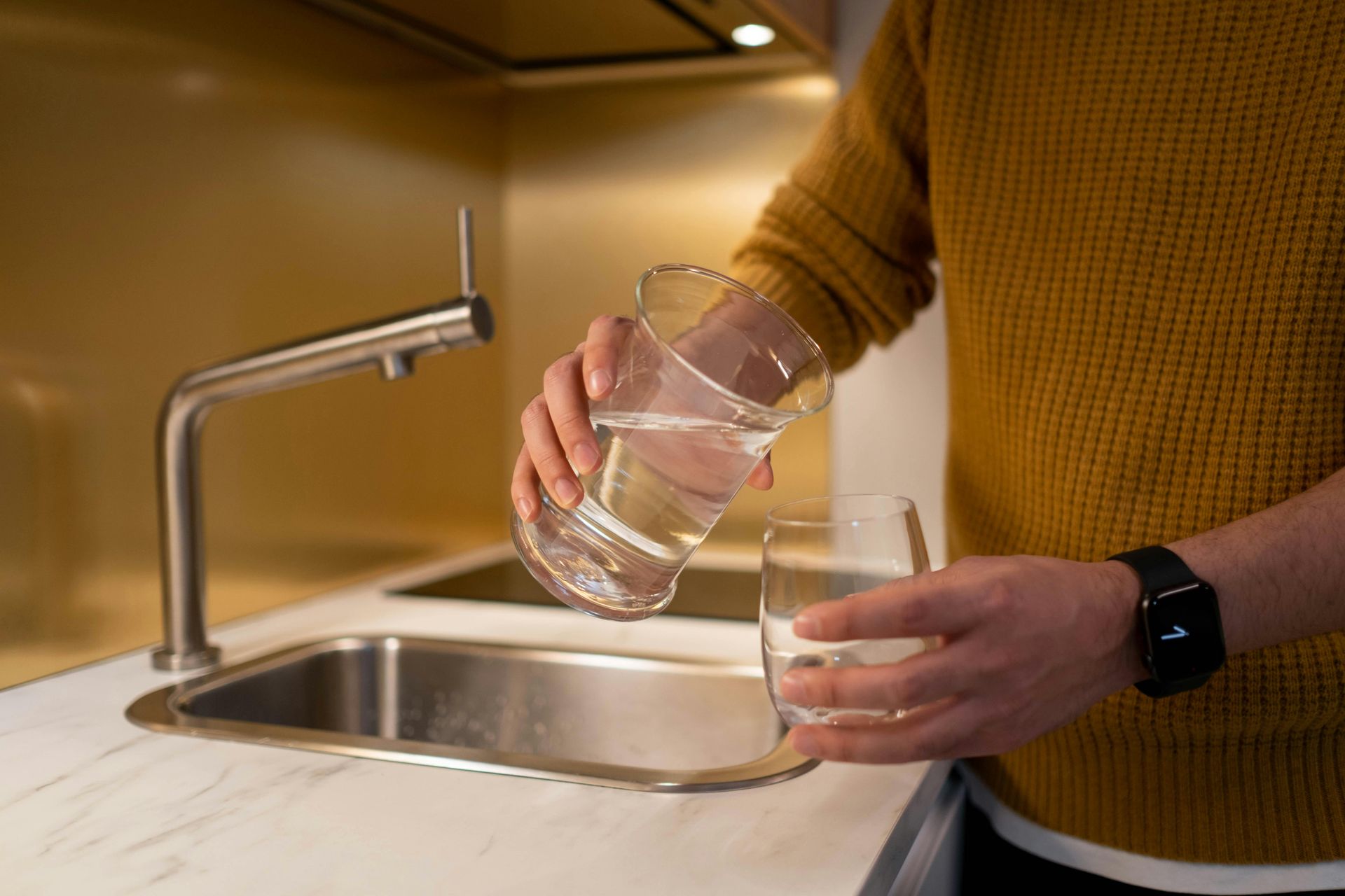 A man is pouring water into a glass in a kitchen.