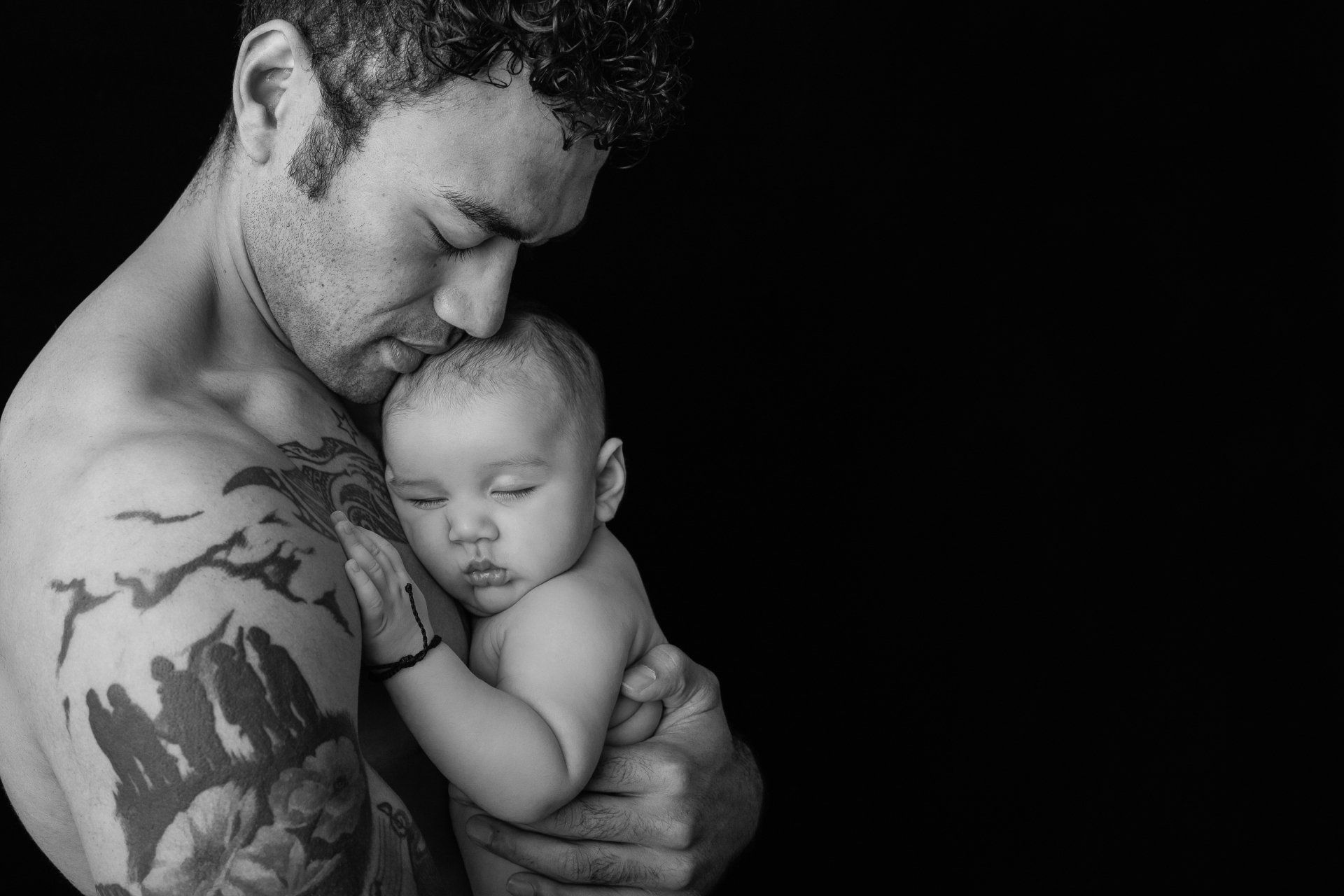 Black and white portrait of a young Tongan man holding his sleeping baby