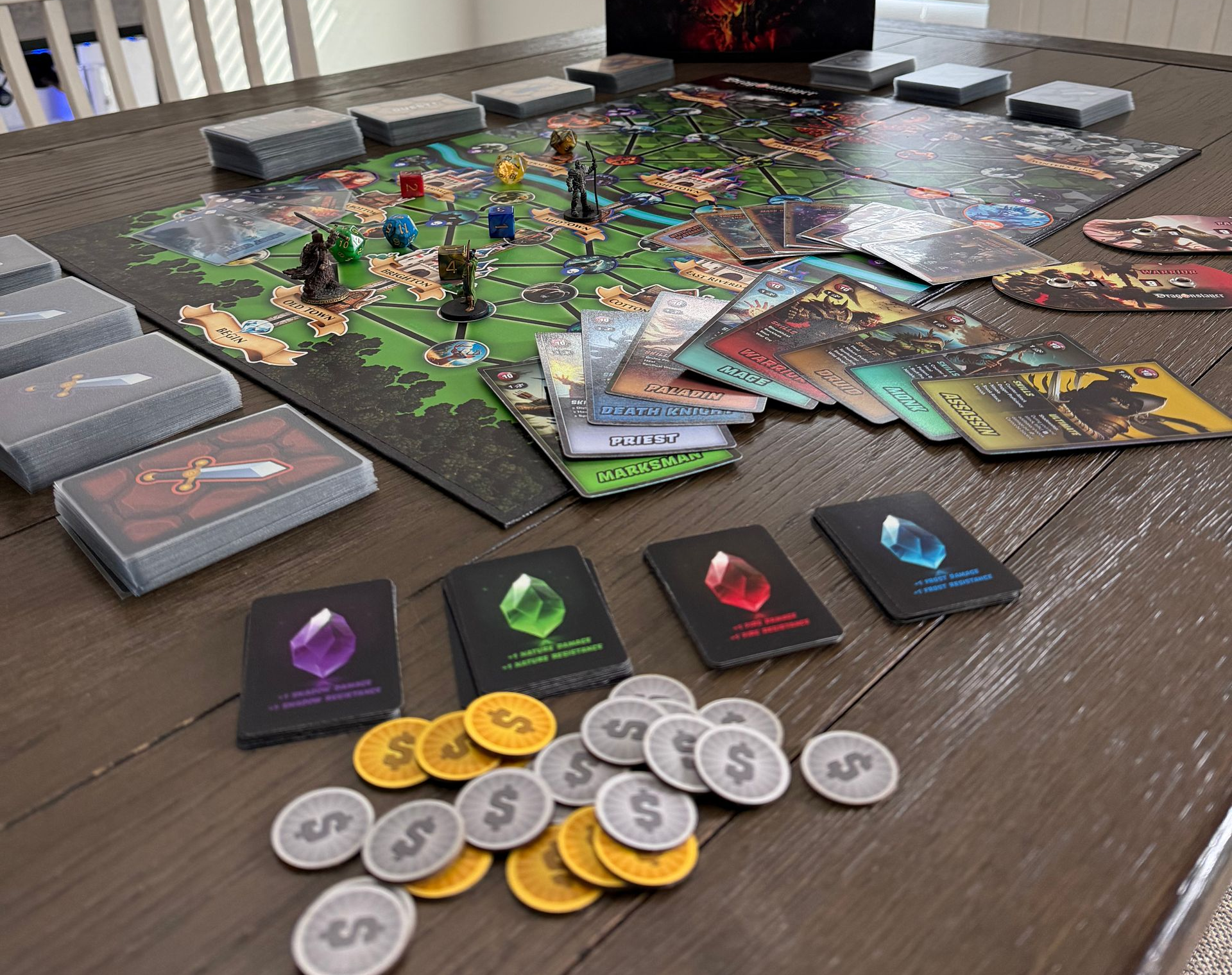 Board game setup on a table, featuring cards, tokens, game board with miniature figures.