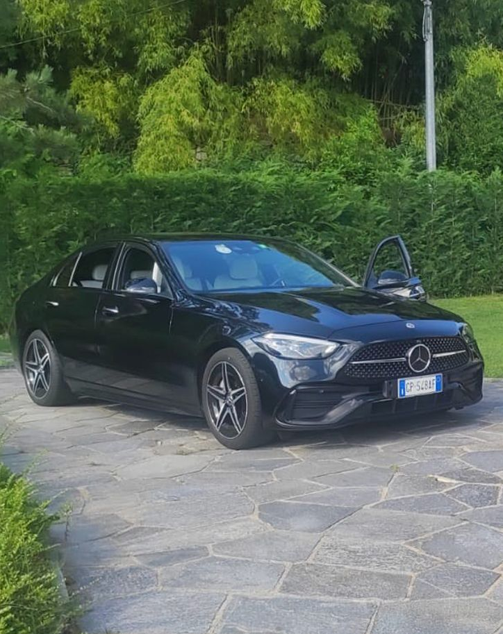 Berlina Mercedes nera parcheggiata su una superficie in pietra, portiera aperta, alberi sullo sfondo.