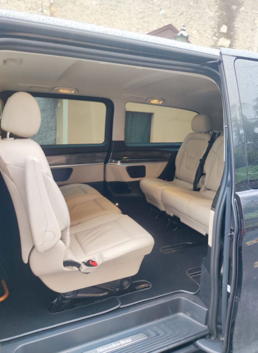 Interno di un furgone Mercedes-Benz nero con sedili in pelle color crema. La portiera laterale è aperta, rivelando l'abitacolo.