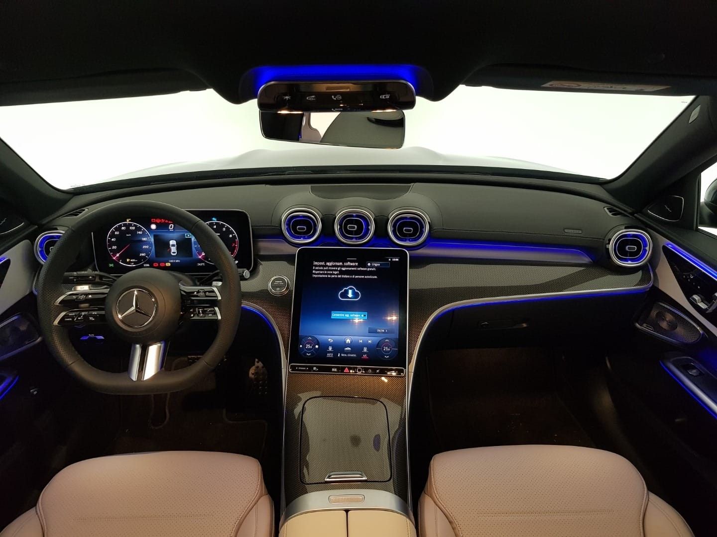Vista interna del cruscotto di un'auto Mercedes-Benz con un grande touchscreen centrale, volante e illuminazione ambientale blu.