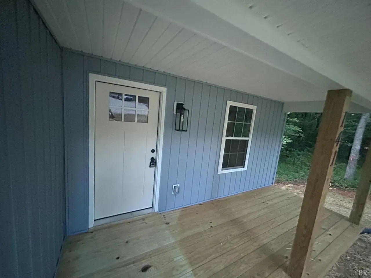 A light blue house exterior featuring a white front door and a window on a wooden porch under an overhanging roof.