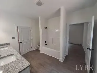 A modern bathroom with a granite vanity, white bathtub shower combo, and open doorways to other rooms.