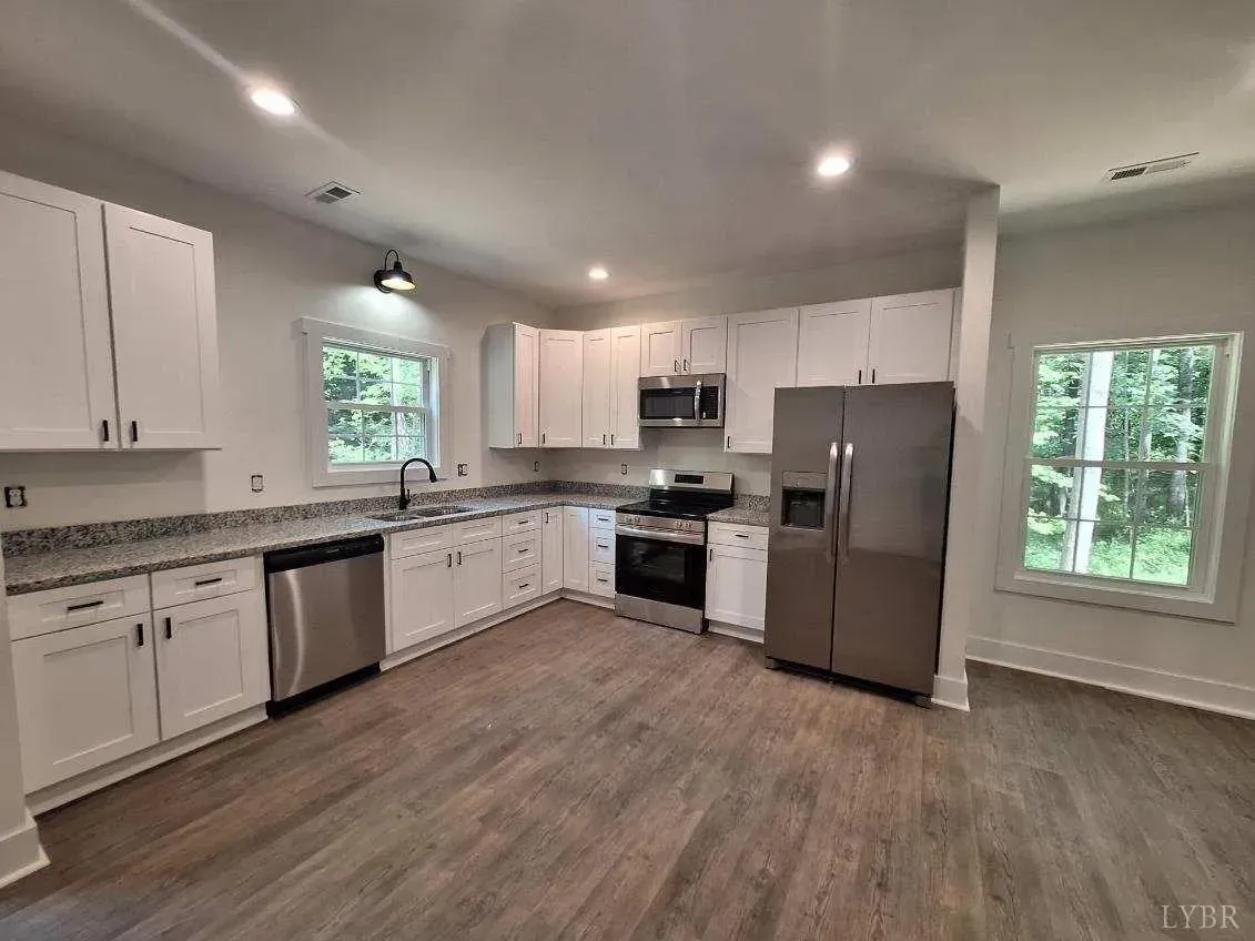 Modern kitchen featuring white cabinets, gray countertops, stainless steel appliances, and wood-look flooring.