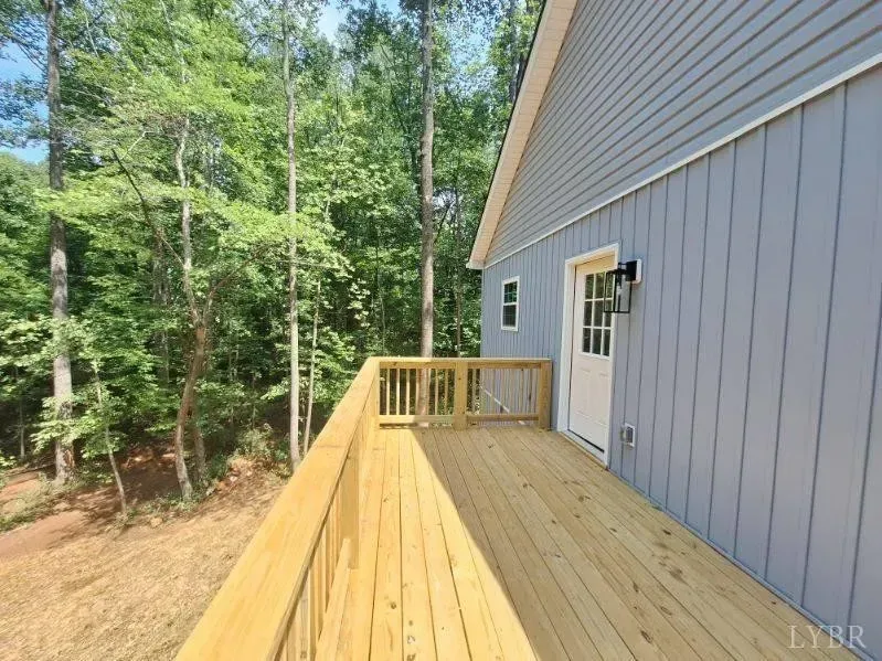 A wooden deck overlooking a wooded area next to a blue-sided house with a white door.