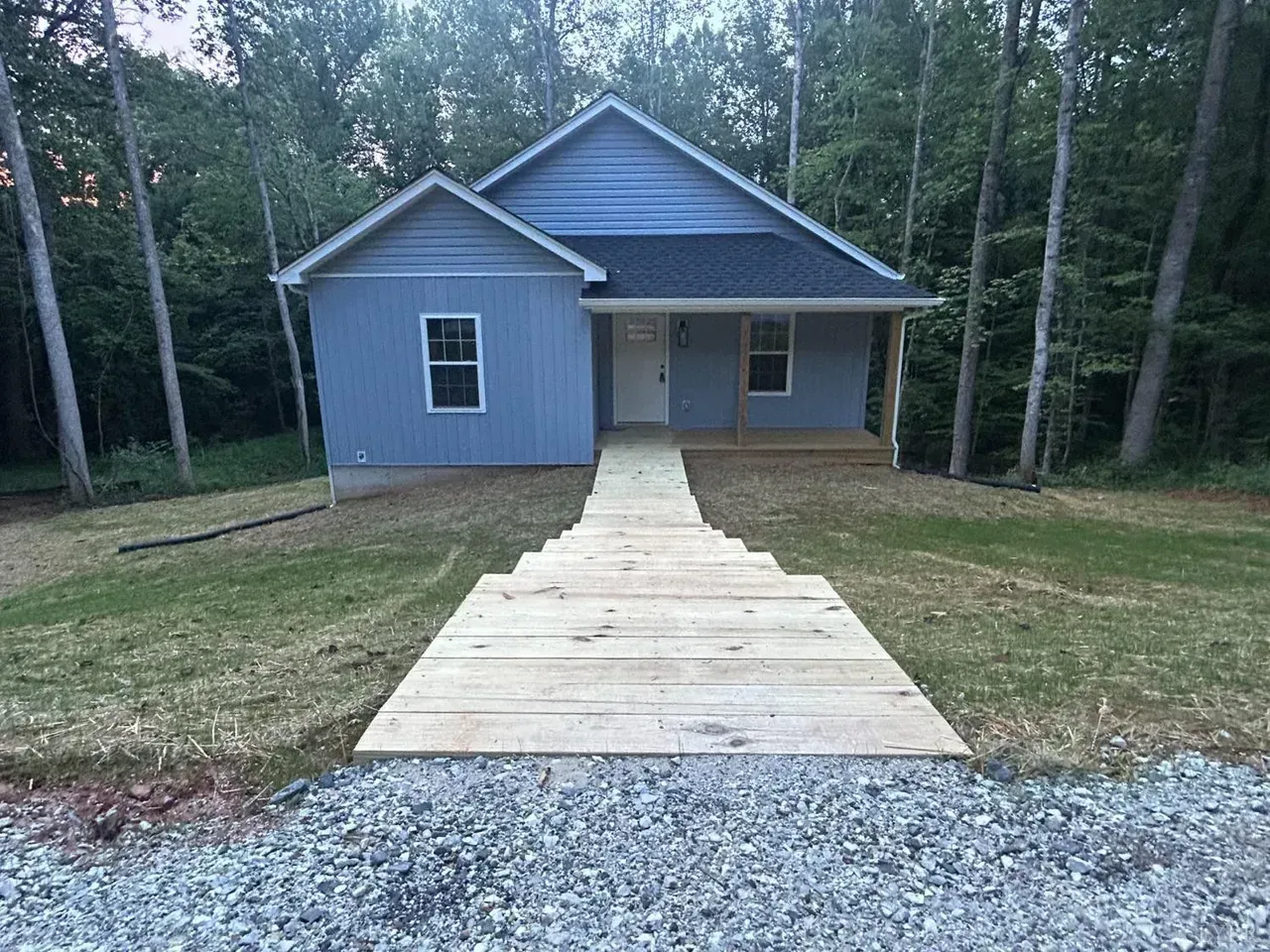 A light blue house set in a wooded area with a wide, tiered wooden walkway leading up to the front porch.